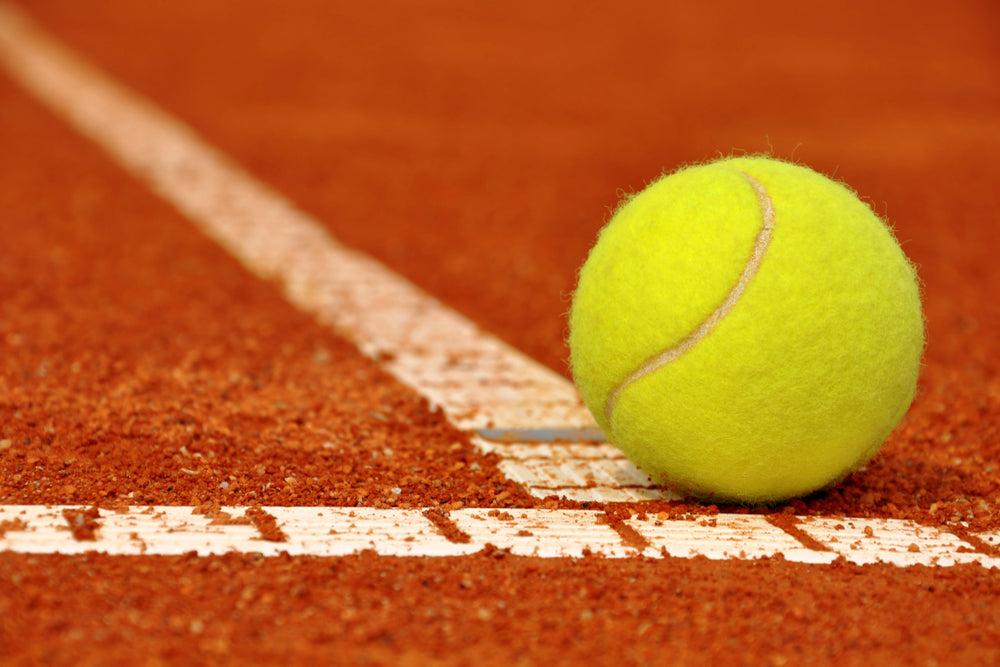 Yellow tennis ball on line of red clay tennis court